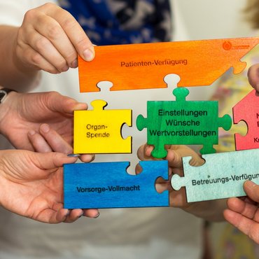 Verschiedenfarbige und beschriftete Puzzleteile werden an das mittlere Puzzleteil mit der Aufschrift 'Einstellungen, Wünsche, Wertvorstellungen' gehalten