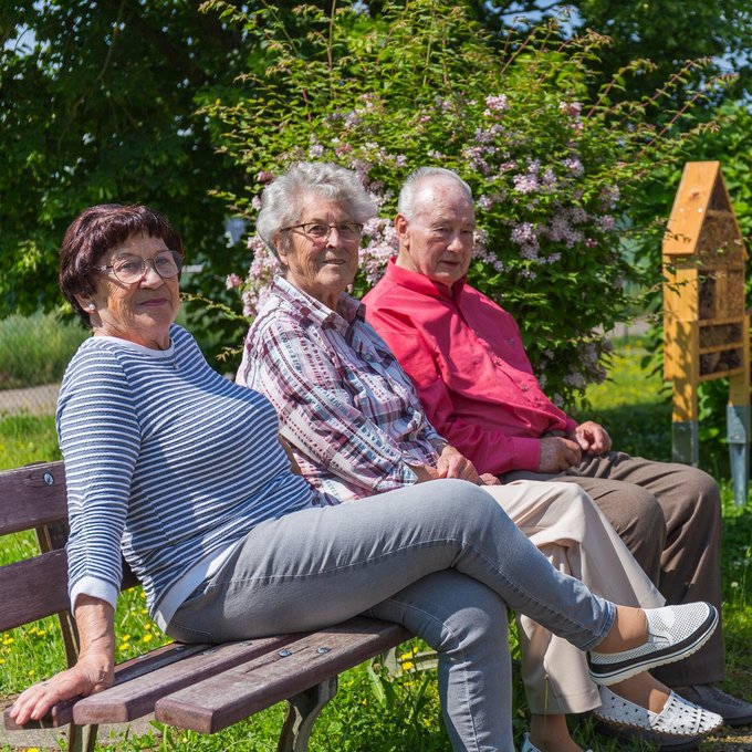 Gäste der Tagespflege Mülsen sitzen auf einer Bank im Garten und genießen das sonnige Wetter
