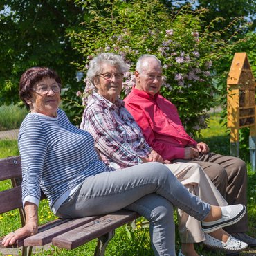 Gäste der Tagespflege Mülsen sitzen auf einer Bank im Garten und genießen das sonnige Wetter