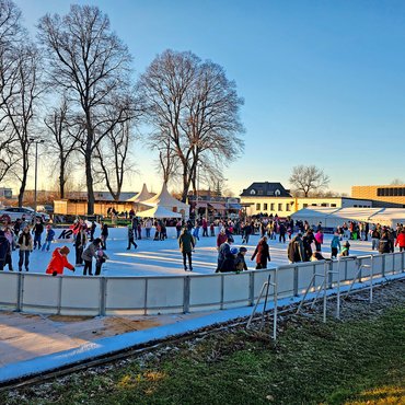 Menschen fahren Schlittschuh auf einer Eisbahn im Freien.