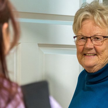 Zuhause wohnen und gut versorgt werden Eine Seniorin empfängt lächelnd die Mitarbeiterin des Pflegedienstes an ihrer Wohnungstür