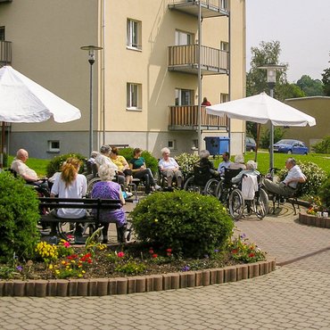 Bewohner sitzen im Sommer vor dem Haus des Betreuten Wohnens