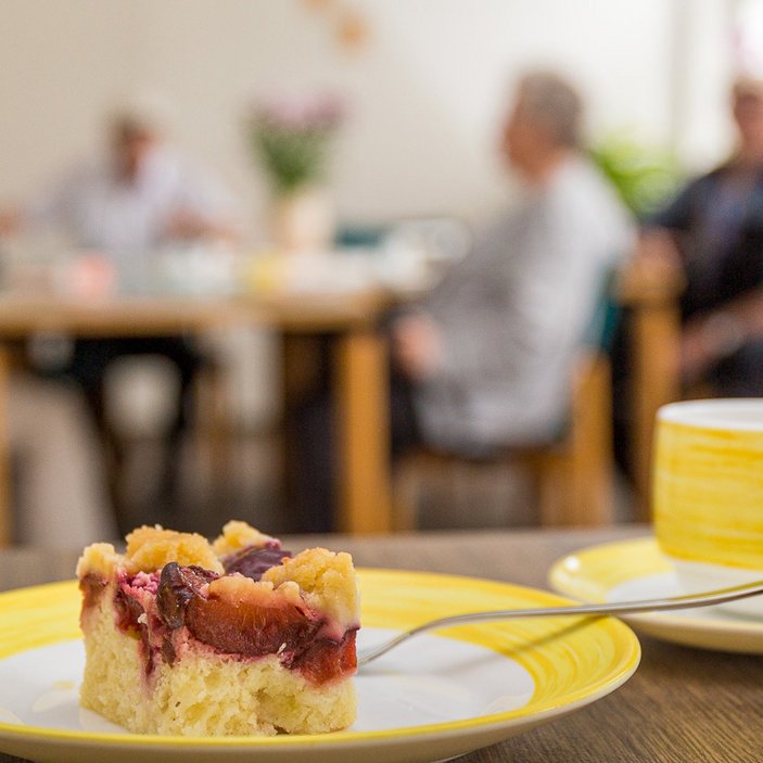 Kaffeetasse und Kuchen vor dem Hintergrund von Gästen der Tagespflege
