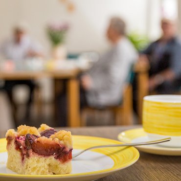 Kaffeetasse und Kuchen vor dem Hintergrund von Gästen der Tagespflege