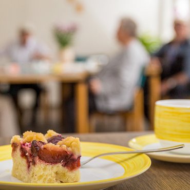 Kaffeetasse und Kuchen vor dem Hintergrund von Gästen der Tagespflege