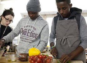 Zwei junge Männer afrikanischer Herkunft bereiten zusammen mit einer Mitarbeiterin Salat vor