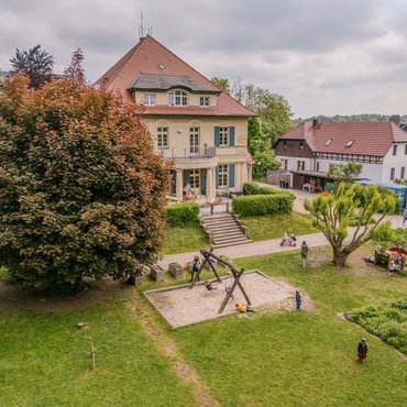 Blick auf eine alte Villa mit großem Garten, in dem Kinder spielen