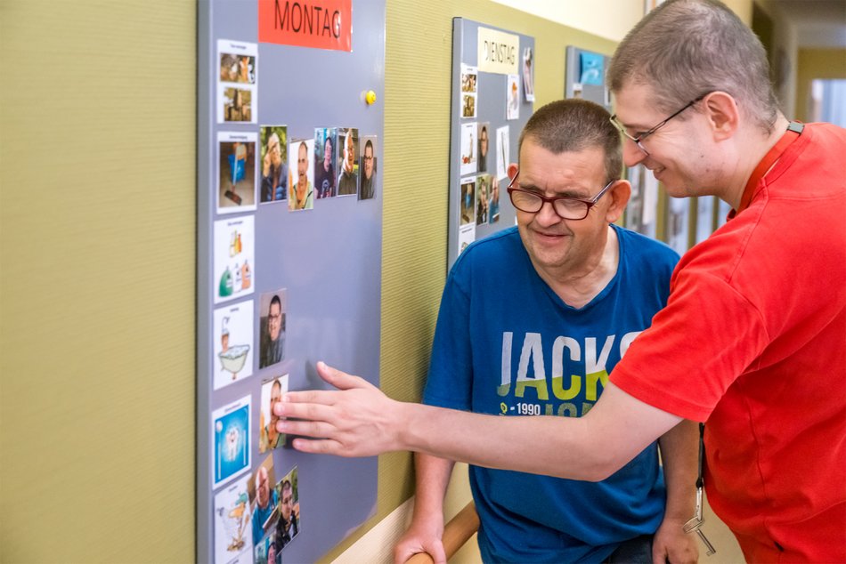 Zwei Männer kleben einen Zettel an den Wochenplan