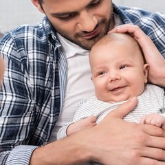 Ein lächelndes Kind auf dem Schoß seines Vaters. Die Mutter lächelt die Beiden an