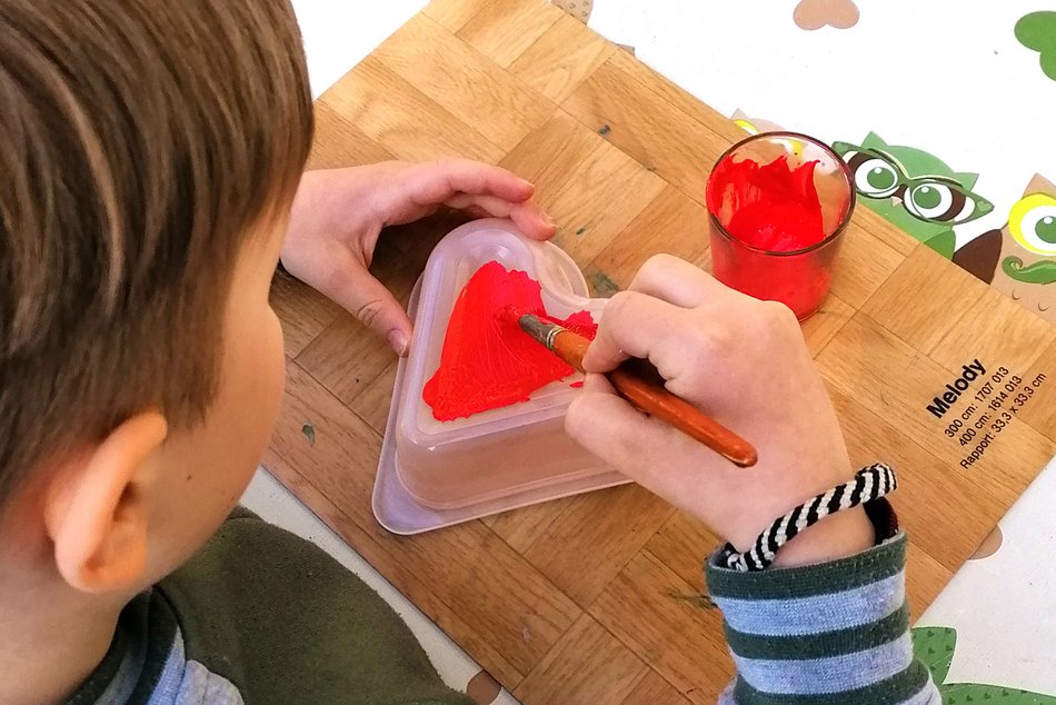 Ein Junge bemalt eine Vorlage mit einem roten Herz