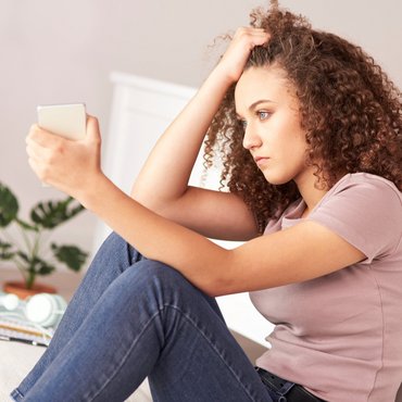Eine junge Frau schaut verzweifelt auf ihr Telefon