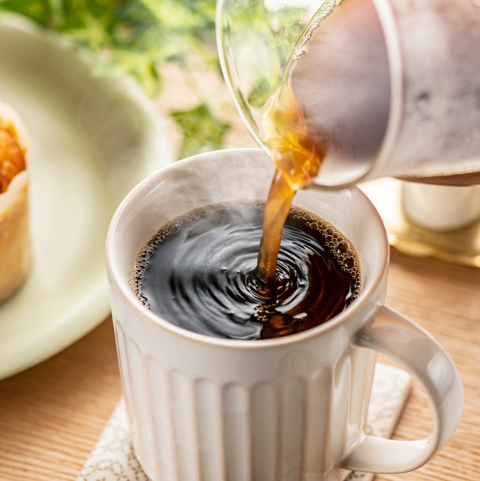 Aus einer Kaffeekanne wird frischer Kaffee in eine Tasse gegossen.