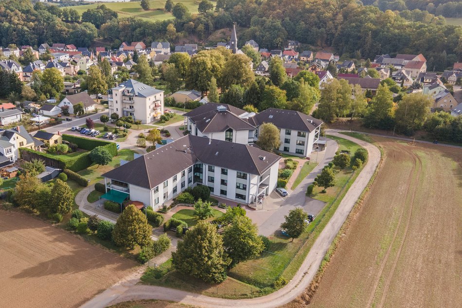 Luftaufnahme vom Jakobushaus mit weißer Fassade und dunkelgrauem Dach. Im Hintergrund ist die Kirche St. Jacob und Häuser von Mülsen zu sehen.