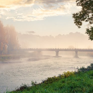 Ein großer Fluss mit Brücke und Bäumen mit Herbstlaub im Nebel