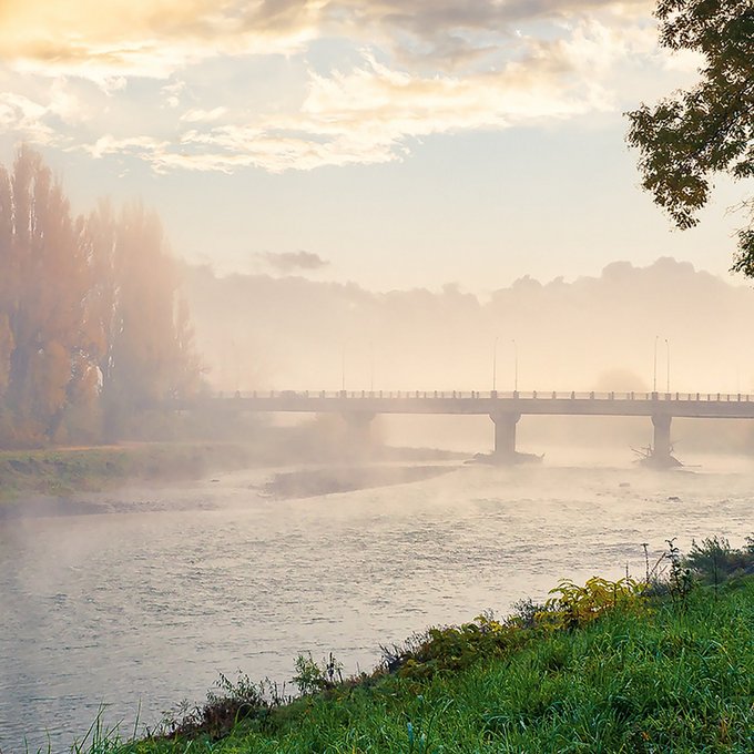 Ein großer Fluss mit Brücke und Bäumen mit Herbstlaub im Nebel
