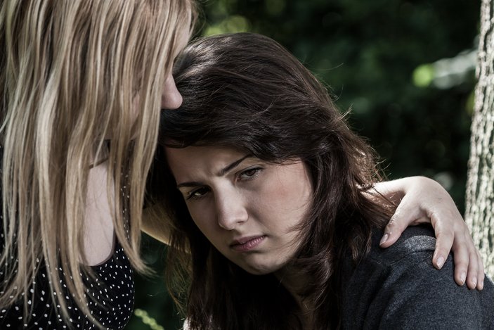 Eine traurige Teenagerin lehnt ihren Kopf an die Schulter einer Frau