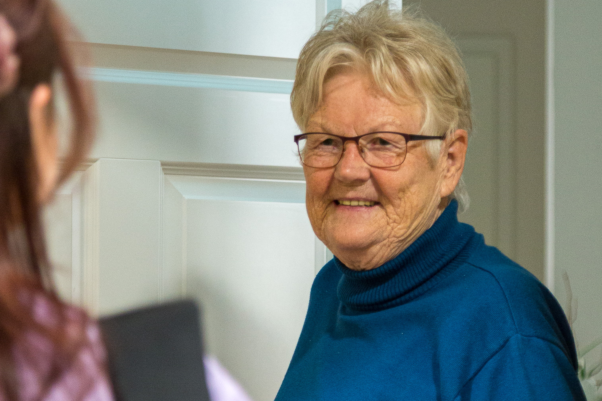 Eine Seniorin empfängt lächelnd die Mitarbeiterin des Pflegedienstes an ihrer Wohnungstür